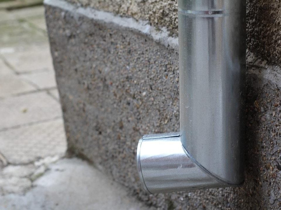 Metal downspout attached to a concrete wall.