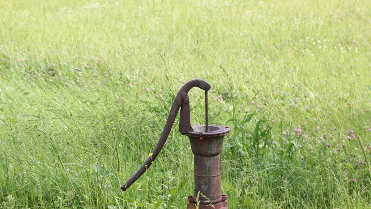 An old, rusted well pump in a green grassy field.