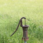 An old, rusted well pump in a green grassy field.