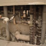 Exposed and corroded plumbing behind a partially demolished wall addresses plumbing issues.