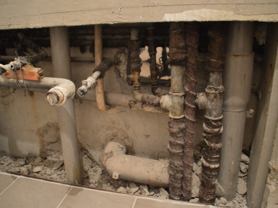 Exposed and corroded plumbing behind a partially demolished wall addresses plumbing issues.