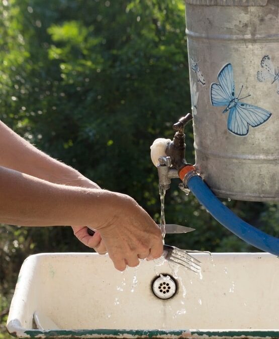 Person washing hands at an outdoor sink, consuming 40 gallons of water from a container with a butterfly sticker.