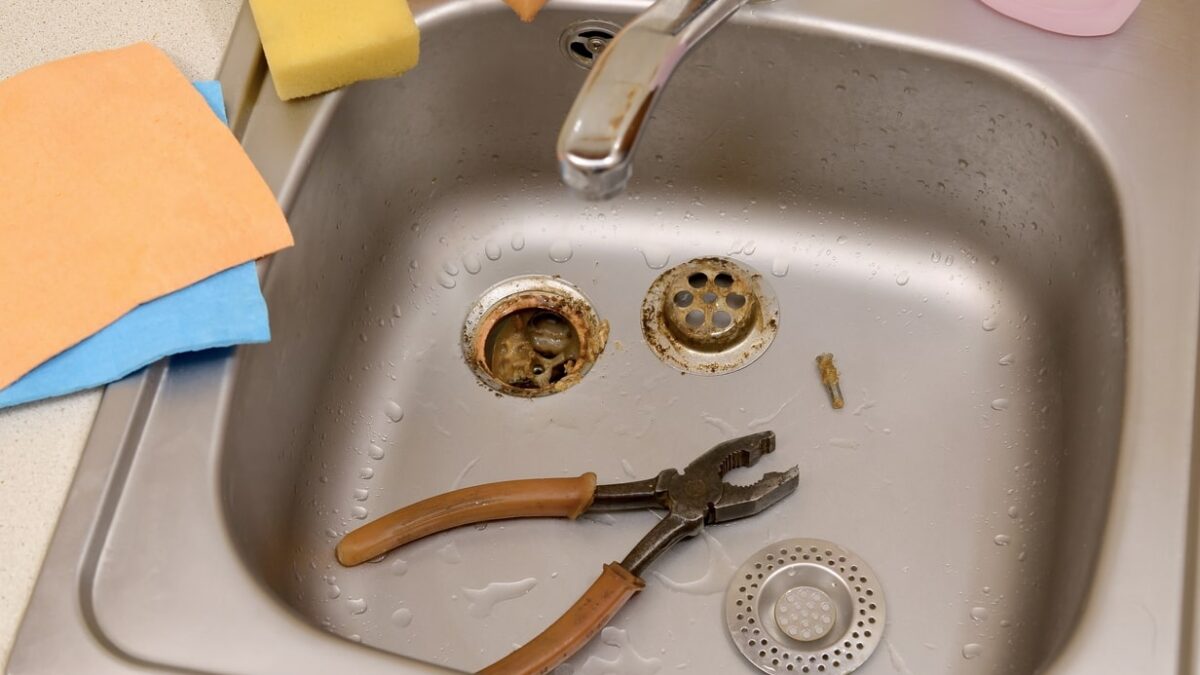 Stainless steel sink with disassembled drain parts and a pair of pliers, indicating plumbing maintenance or repair to fix a gurgling drain.
