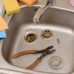 Stainless steel sink with disassembled drain parts and a pair of pliers, indicating plumbing maintenance or repair to fix a gurgling drain.
