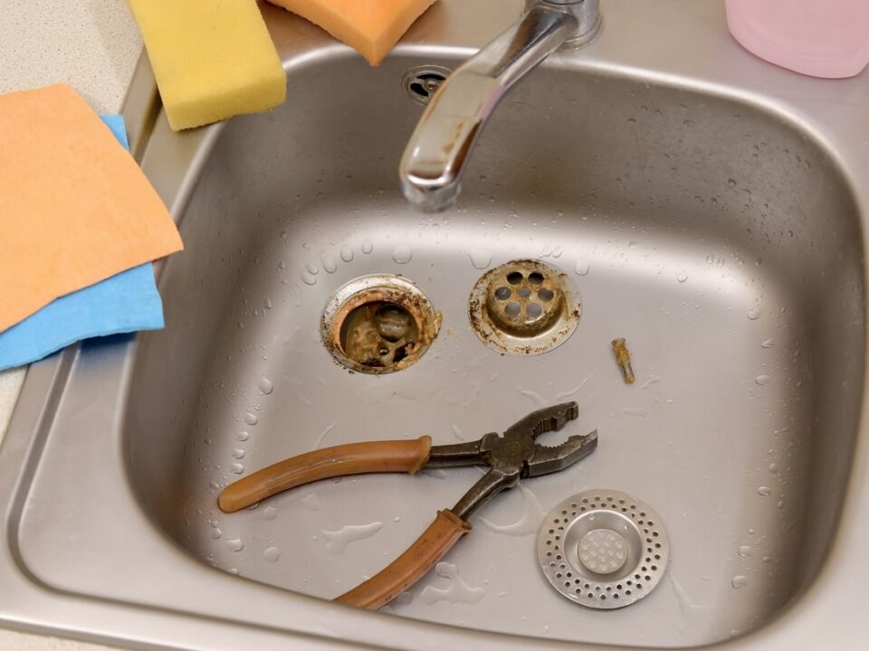 Stainless steel sink with disassembled drain parts and a pair of pliers, indicating plumbing maintenance or repair to fix a gurgling drain.